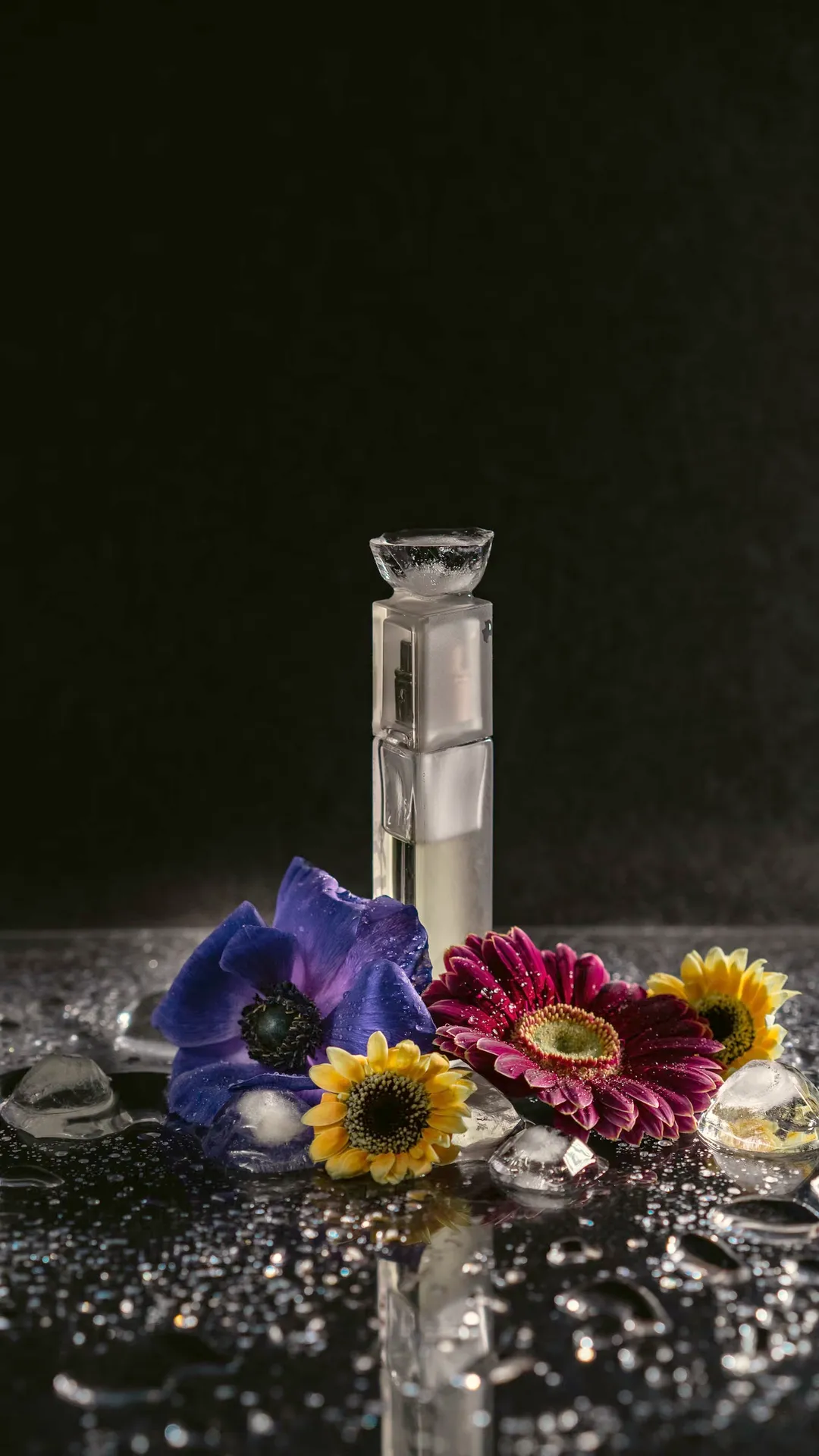 Sculpted perfume bottle with an iris and a gerbera on wet black stone