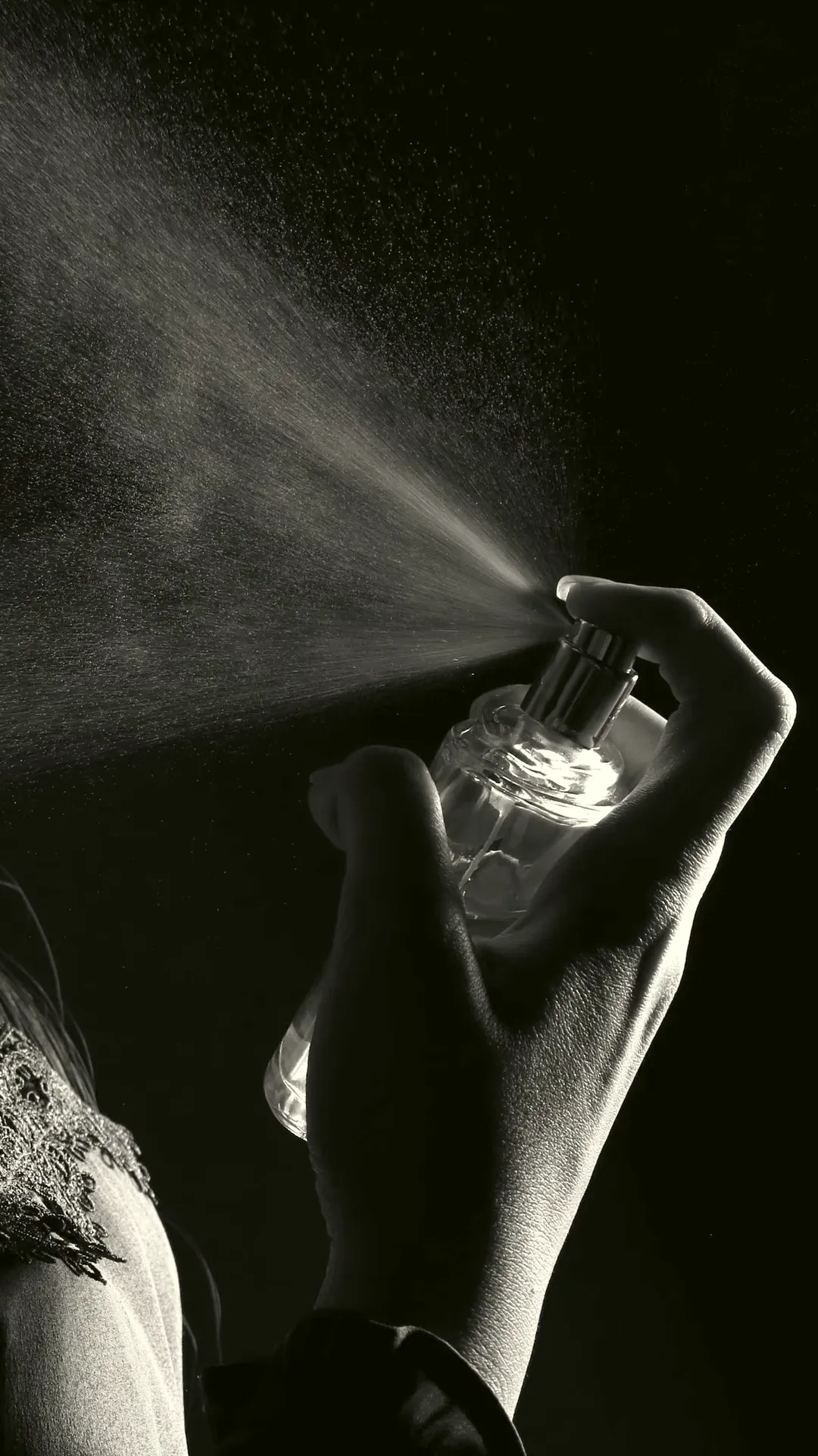 Black and white photo of perfume mist at a neckline, backlit, no face